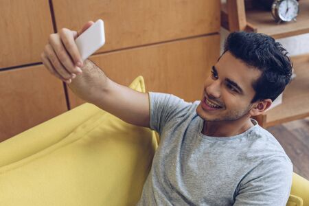 Man smiling and taking selfie with smartphone on sofa