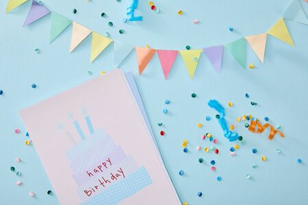 top view of colorful confetti near birthday greeting card on blue backgroundの写真素材