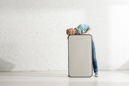 Smiling man standing near huge model of smartphone near white brick wallの写真素材