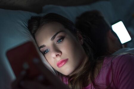 Selective focus of addicted woman using smartphone near man on bed at nightの写真素材