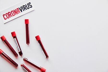 top view of test tubes with blood samples and coronavirus test near paper with coronavirus lettering on whiteの写真素材