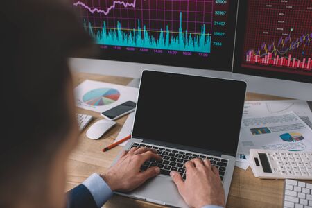 Selective focus of data analyst using laptop near charts on papers and computer monitors on table