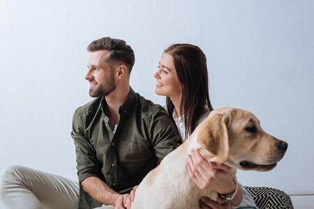 Selective focus of smiling couple looking away near golden retriever on grey backgroundの写真素材