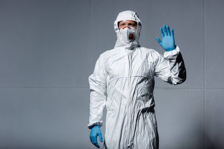 man in personal protective equipment waving hand on grey