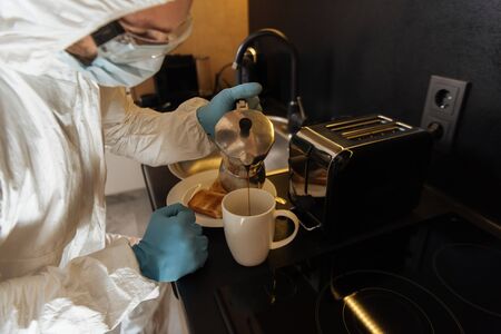 selective focus of man in personal protective equipment pouring coffee in cup near toast bread and...