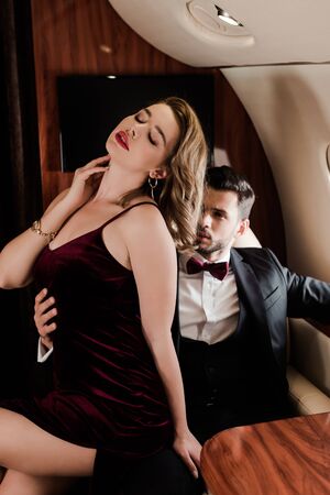 handsome man touching sexy, elegant woman sitting on his laps in planeの写真素材