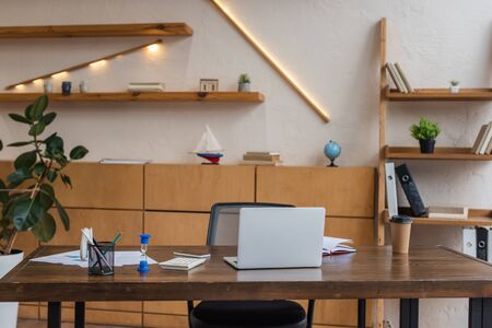 Table with laptop, hourglass and pen holder in office