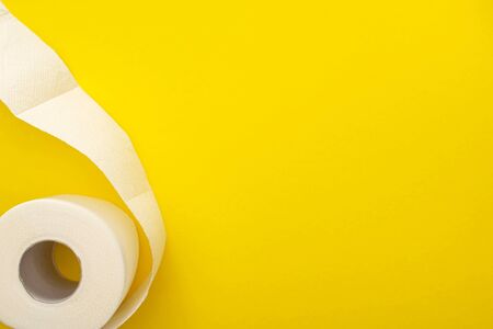 top view of white toilet paper roll on yellow background with copy space