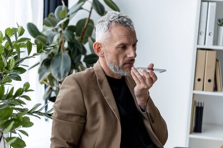 businessman recording voice message near green plants in office
