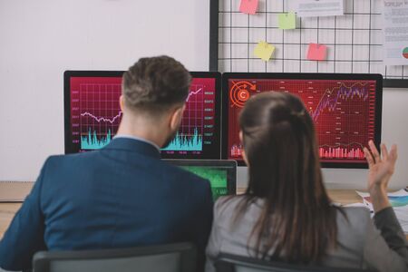 Back view of data analysts working on strategy of security with graphs on computer monitors