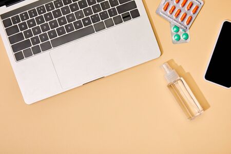 top view of laptop and smartphone with blank screen near pills and bottle with hand sanitizer on...
