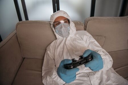 KYIV, UKRAINE - APRIL 11, 2020: man in personal protective equipment and medical mask playing video...