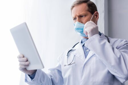 selective focus of mature doctor in medical mask using digital tablet on whiteの写真素材