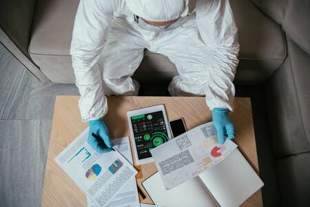 top view of man in personal protective equipment working near digital tablet with charts and graphs and smartphone with blank screenの写真素材