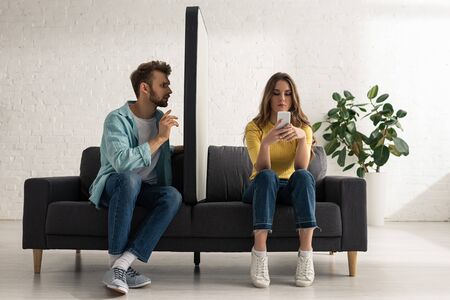 Man sitting near model of smartphone and addicted girlfriend chatting on couch