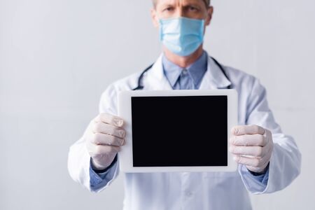 selective focus of mature doctor in medical mask holding digital tablet with blank screen isolated on whiteの写真素材