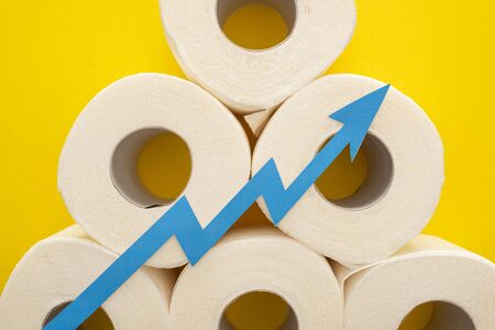 top view of blue arrow on white toilet paper rolls on yellow background