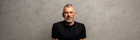 panoramic shot of handsome man looking at camera on grey