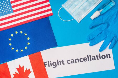 Top view of card with flight cancellation lettering near medical mask and flags of countries on blue surfaceの写真素材