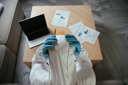 top view of man in personal protective equipment touching head near laptop with blank screen and credit cardsの写真素材