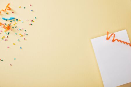 top view of festive colorful confetti near blank paper on beige background