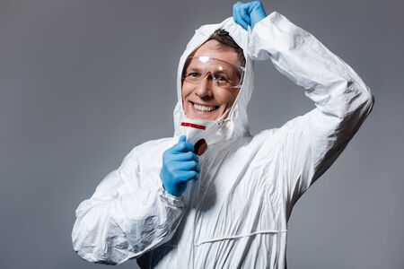 cheerful and mature man in hazmat suit and goggles isolated on grey