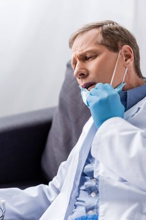 exhausted and mature doctor touching medical maskの写真素材