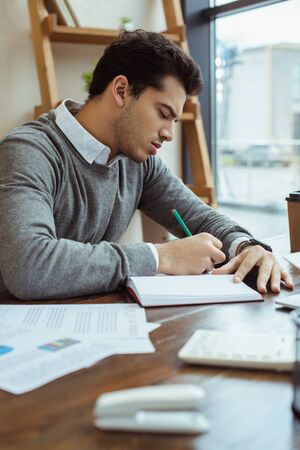 Selective focus of businessman writing in notebook at table in officeの写真素材