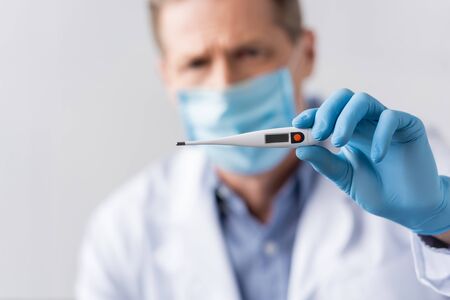 selective focus of mature doctor in latex glove holding digital thermometer isolated on greyの写真素材