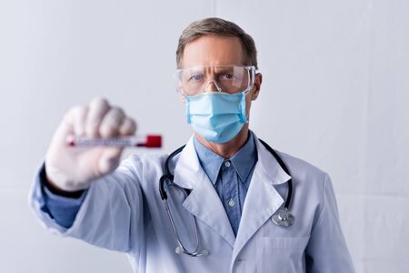 selective focus of mature doctor in medical mask holding test tube with blood sample on greyの写真素材