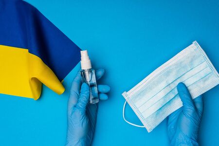 Top view of doctor holding bottle with hand sanitizer and medical mask near flag of ukraine on blue backgroundの写真素材