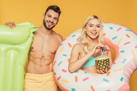 handsome shirtess man holding inflatable mattress near attractive blonde girl with swim ring and...