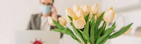 selective focus of tulips bouquet near businesswoman in medical mask working at home, horizontal imageの写真素材