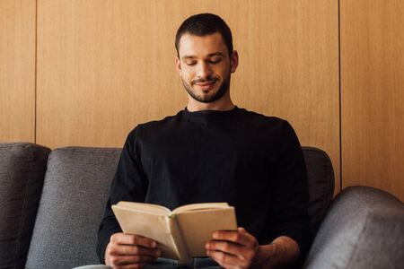 happy and bearded man reading book in living roomの写真素材