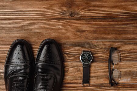 Flat lay with mens black shoes, wristwatch and glasses on wooden backgroundの写真素材