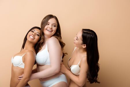 happy plus size multicultural girls in bras isolated on beigeの写真素材