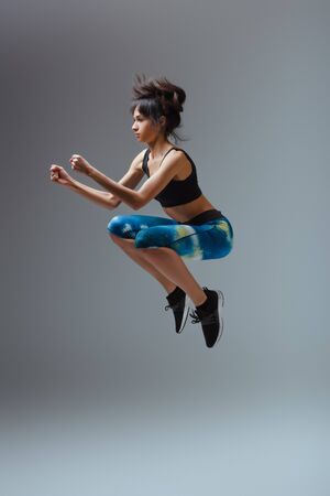 attractive african american woman in sportswear jumping on grey
