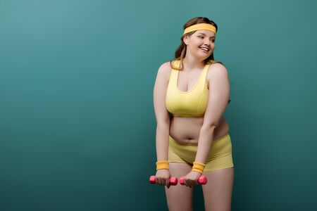 Plus size sportswoman training with dumbbells and smiling on green