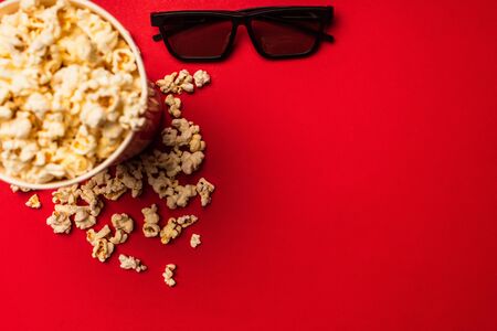 Top view of sunglasses near bucket with tasty popcorn on red backgroundの写真素材