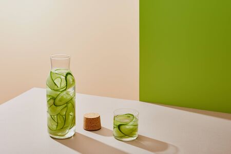 high angle view of cork, glass and bottle filled with water and sliced cucumbers on table on beige...