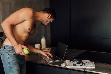 muscular freelancer holding apple and using laptop with blank screenの写真素材