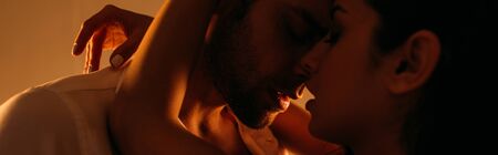 Passionate woman hugging businessman with closed eyes in bedroom, panoramic shot