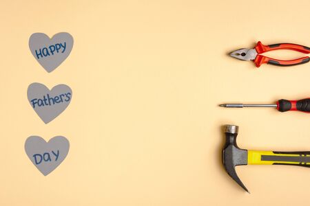 Flat lay with hammer, screwdriver, pliers and paper hearts with lettering happy fathers day on beige...