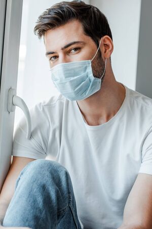 Man in medical mask looking at camera near windowの写真素材