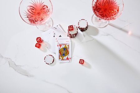 high angle view of playing cards, glasses of cocktail, dice and casino chips on white background