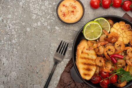 top view of fried shrimps with sauce, fork, grilled toasts, vegetables and lime on grey concrete...
