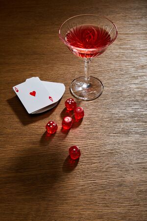 high angle view of glass of cocktail near deck of cards and dice on wooden background