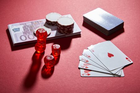 high angle view of playing cards, dice, casino chips and banknotes on red