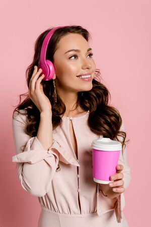 happy girl listening music in wireless headphones and holding paper cup on pinkの写真素材