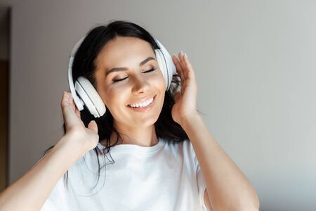 cheerful young woman with closed eyes listening music with headphones at homeの写真素材